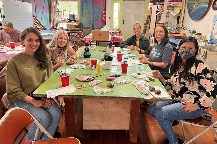 Miembros de la comunidad, incluida Teresa Lavagnino, reunidos alrededor de una mesa pintando rocas.
