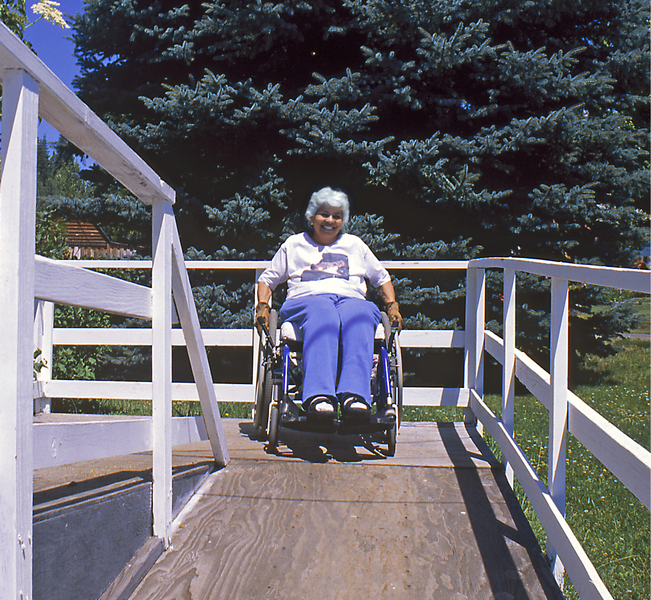 Person in wheelchair uses an outdoor ramp providing home access.  